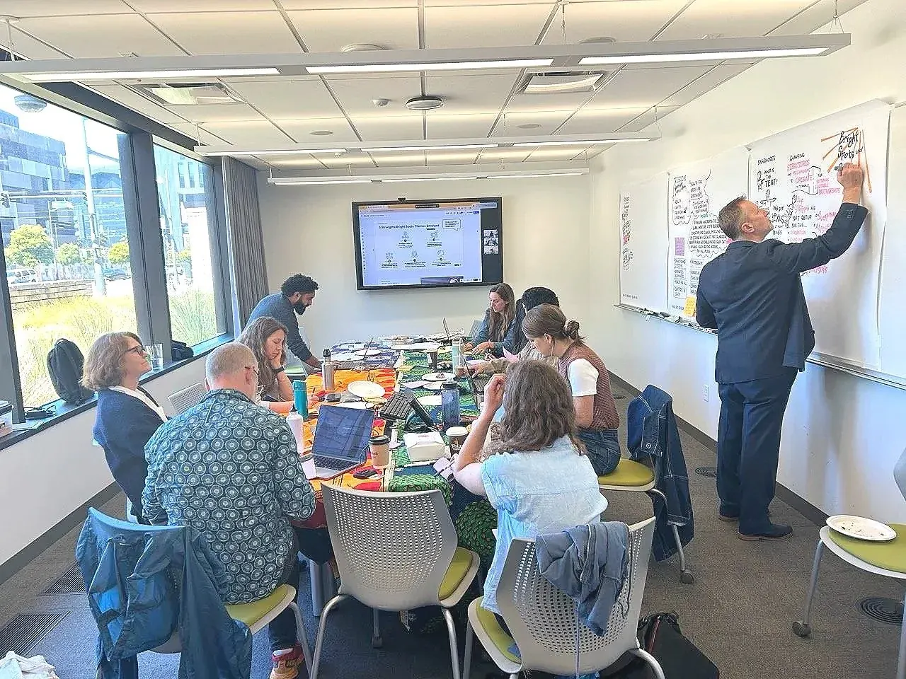 A Caravann facilitator graphic recording on wall panels while a leadership team works around a table